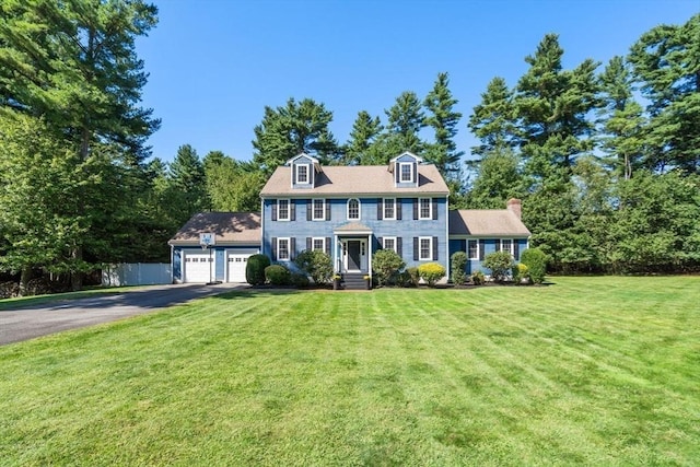 colonial home with a garage, a front yard, driveway, and fence