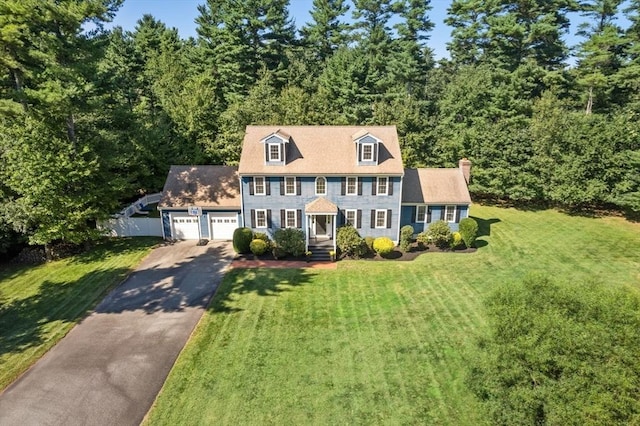 colonial home with aphalt driveway, an attached garage, fence, a front lawn, and a chimney