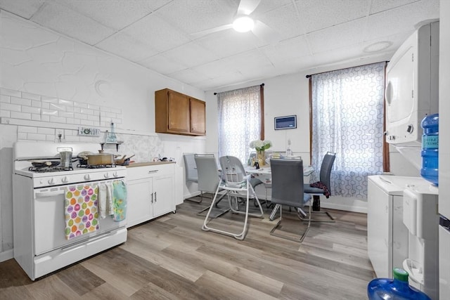 kitchen with stacked washer / drying machine, brown cabinetry, a drop ceiling, white range with gas stovetop, and light wood-type flooring