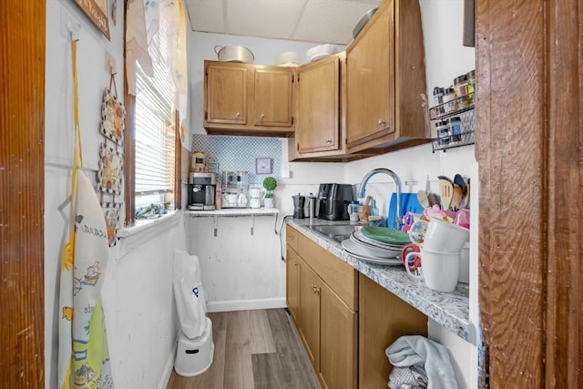 kitchen with brown cabinets, a sink, light countertops, baseboards, and wood finished floors