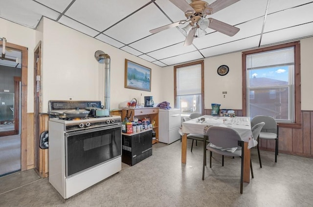 kitchen featuring a wainscoted wall, white gas range, a ceiling fan, washer / dryer, and a drop ceiling