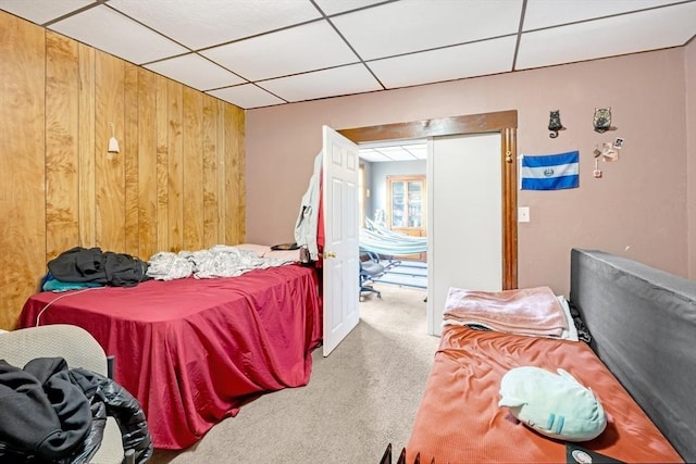 bedroom featuring wood walls, carpet, and a drop ceiling