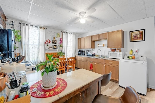 kitchen with light wood finished floors, freestanding refrigerator, a ceiling fan, washer / dryer, and white microwave