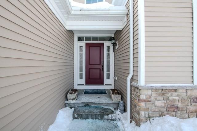 snow covered property entrance with stone siding