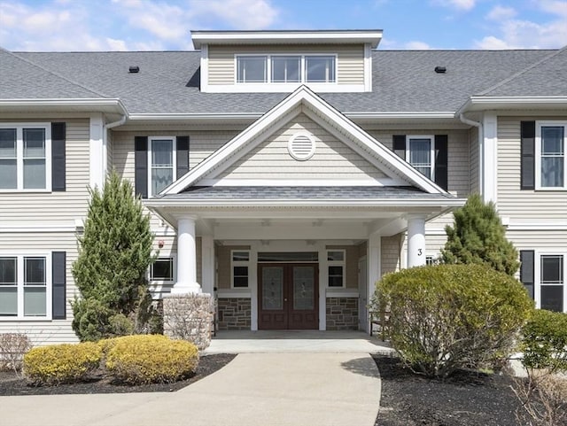 view of exterior entry with roof with shingles, french doors, and driveway