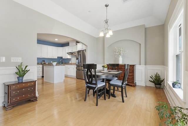 dining room featuring arched walkways, wainscoting, a chandelier, light wood-style floors, and a decorative wall