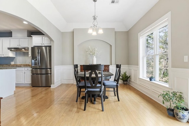 dining area with arched walkways, a wainscoted wall, light wood-type flooring, and a chandelier