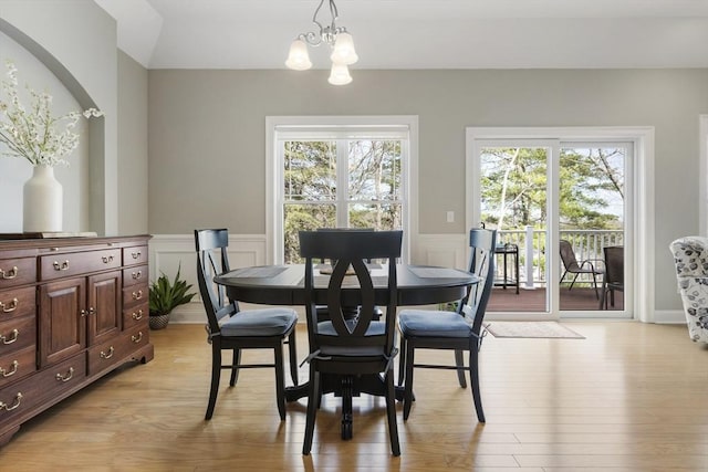 dining room featuring light wood-style flooring, a decorative wall, a wainscoted wall, and a chandelier