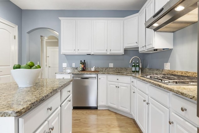 kitchen with a sink, arched walkways, stainless steel appliances, white cabinetry, and under cabinet range hood