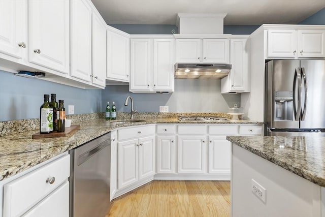 kitchen featuring light wood-type flooring, white cabinetry, under cabinet range hood, a sink, and appliances with stainless steel finishes