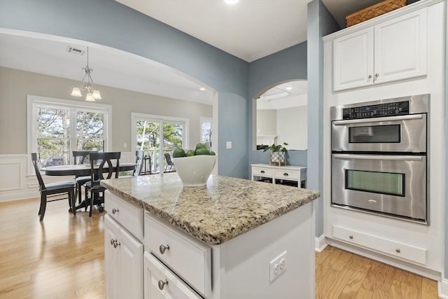kitchen featuring stainless steel double oven, light wood-style floors, arched walkways, a center island, and visible vents