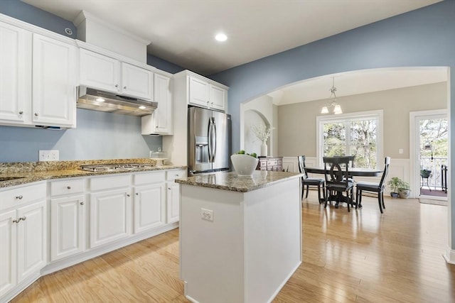 kitchen with light wood-style floors, white cabinetry, under cabinet range hood, arched walkways, and stainless steel appliances