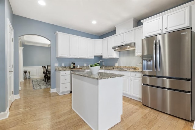 kitchen featuring white cabinets, arched walkways, light wood-style flooring, stainless steel appliances, and under cabinet range hood