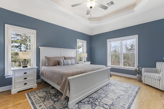 bedroom with ceiling fan, visible vents, baseboards, a tray ceiling, and light wood-style flooring
