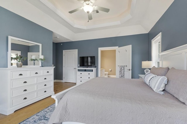 bedroom featuring ceiling fan, visible vents, light wood-type flooring, connected bathroom, and a tray ceiling
