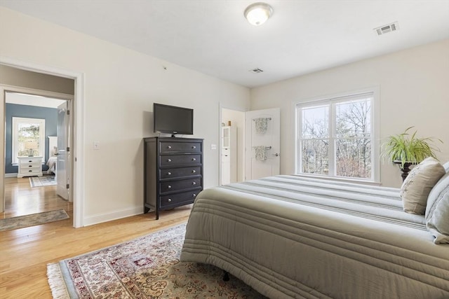 bedroom with baseboards, visible vents, multiple windows, and light wood-style floors