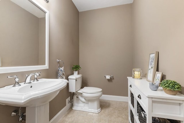 half bath with baseboards, a sink, tile patterned floors, and toilet