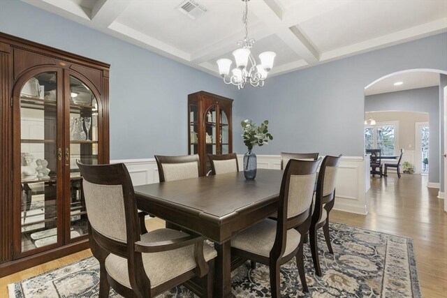 dining room featuring an inviting chandelier, arched walkways, a wainscoted wall, visible vents, and coffered ceiling