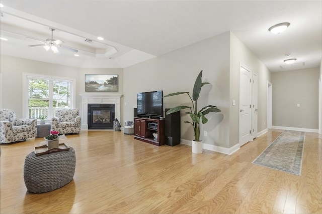 living area with a glass covered fireplace, baseboards, a ceiling fan, and wood finished floors