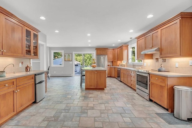 kitchen featuring a baseboard radiator, under cabinet range hood, a sink, appliances with stainless steel finishes, and glass insert cabinets