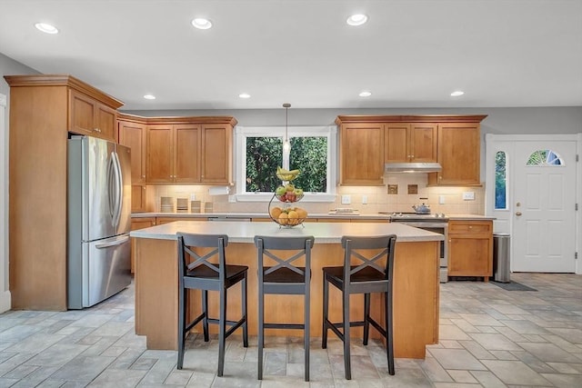 kitchen with light countertops, appliances with stainless steel finishes, stone finish flooring, a kitchen island, and under cabinet range hood