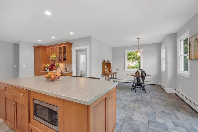 kitchen with light countertops, stainless steel microwave, a baseboard radiator, and brown cabinets