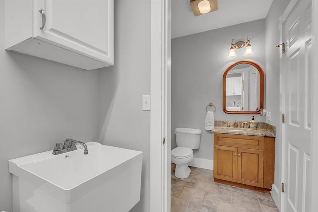 bathroom with toilet, stone finish floor, baseboards, and vanity