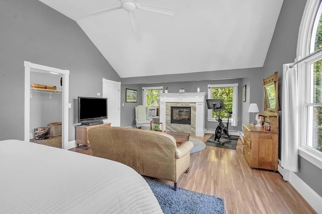 bedroom featuring light wood-style floors, a high end fireplace, high vaulted ceiling, and baseboards