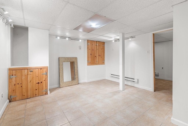 finished below grade area featuring a drop ceiling, a baseboard heating unit, and baseboards