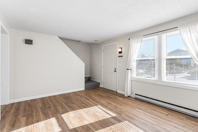 interior space featuring stairway, wood finished floors, baseboards, a baseboard radiator, and a textured ceiling