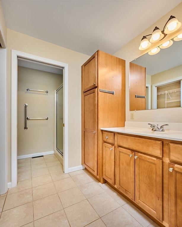 full bathroom with a shower with shower door, baseboards, vanity, and tile patterned floors