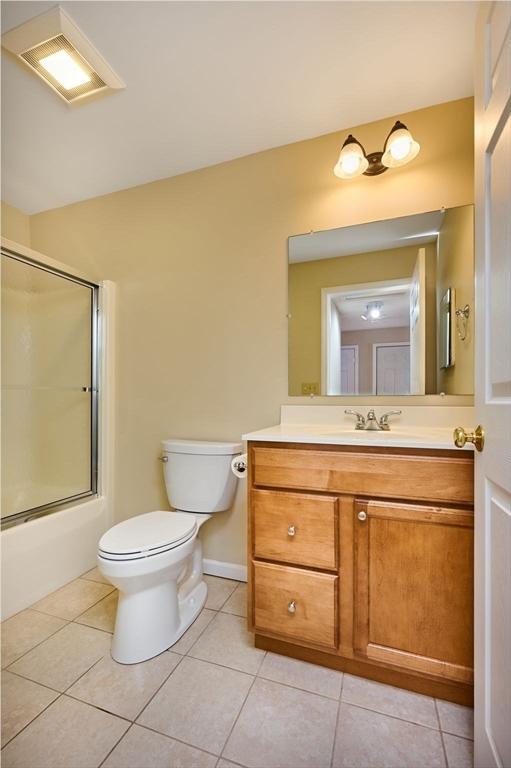 full bath with tile patterned floors, enclosed tub / shower combo, toilet, and vanity