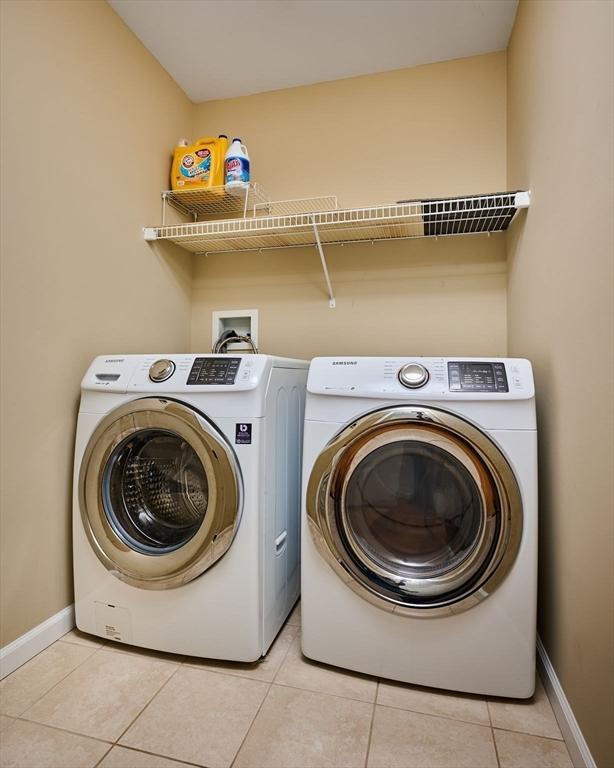 clothes washing area featuring light tile patterned flooring, laundry area, washer and dryer, and baseboards