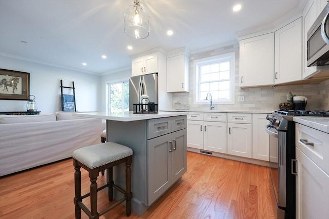 kitchen with appliances with stainless steel finishes, a center island, white cabinetry, gray cabinets, and a breakfast bar area