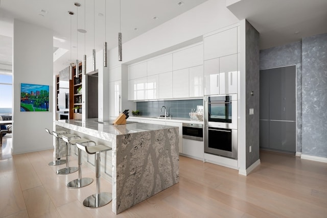 kitchen with white cabinetry, backsplash, decorative light fixtures, a kitchen island, and light hardwood / wood-style floors