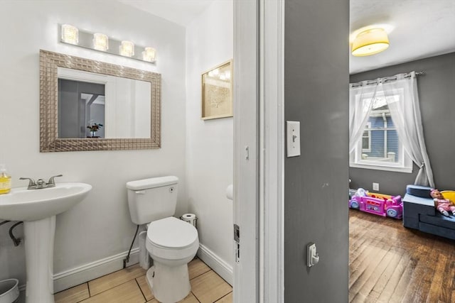 half bath with a sink, wood finished floors, toilet, and baseboards