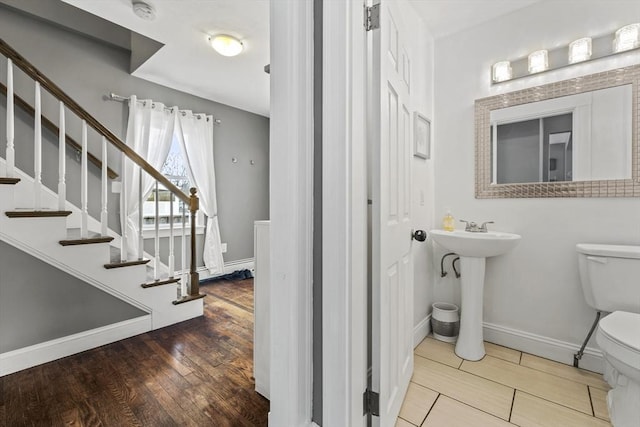 half bathroom with baseboards, a sink, toilet, and wood finished floors