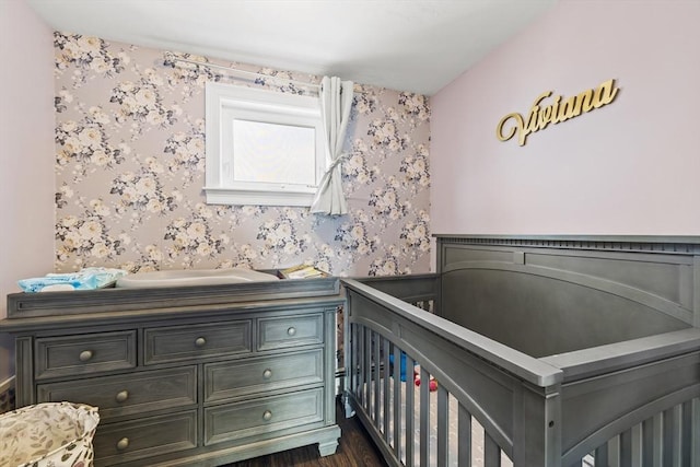 bedroom featuring a crib, wallpapered walls, dark wood-style flooring, and wainscoting