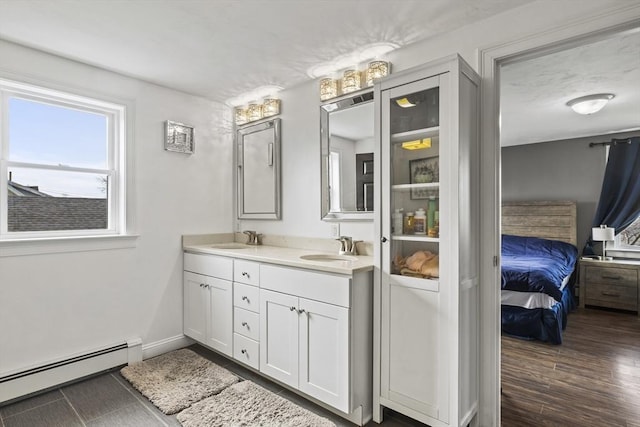 ensuite bathroom featuring double vanity, ensuite bath, wood finished floors, a baseboard heating unit, and a sink