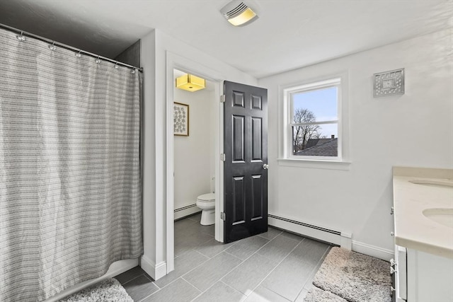 bathroom featuring toilet, double vanity, baseboards, and baseboard heating