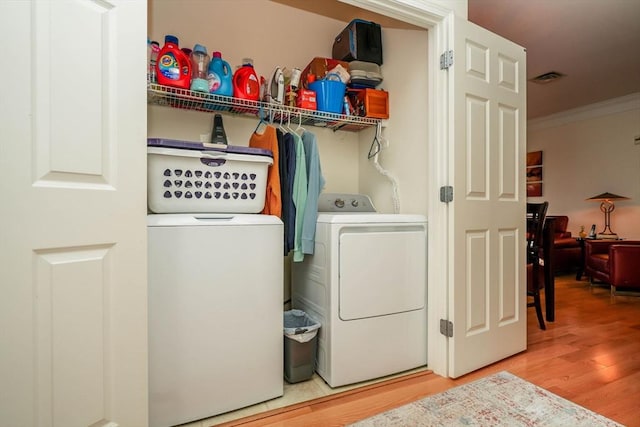 clothes washing area featuring washing machine and dryer, crown molding, and wood-type flooring