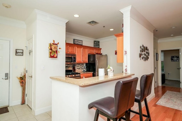 kitchen featuring kitchen peninsula, appliances with stainless steel finishes, crown molding, and a kitchen breakfast bar