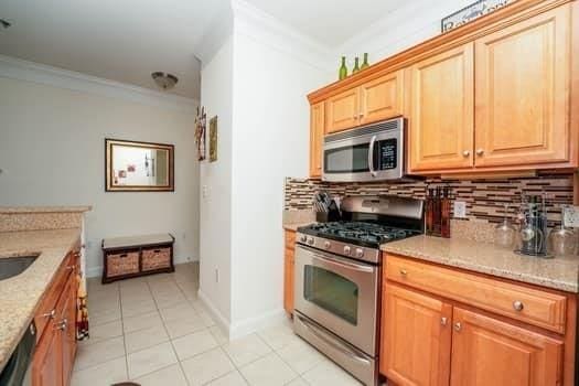 kitchen with light stone countertops, stainless steel appliances, light tile patterned floors, decorative backsplash, and ornamental molding