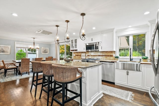 kitchen with white cabinets, dark hardwood / wood-style floors, stainless steel appliances, decorative light fixtures, and a center island