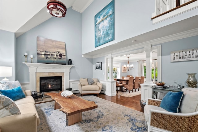 living room with a high ceiling, baseboard heating, wood-type flooring, crown molding, and a chandelier