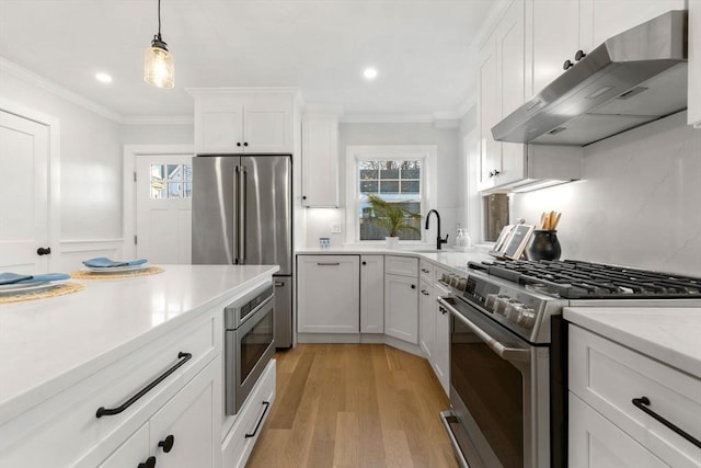 kitchen with appliances with stainless steel finishes, extractor fan, white cabinetry, hanging light fixtures, and light wood-type flooring