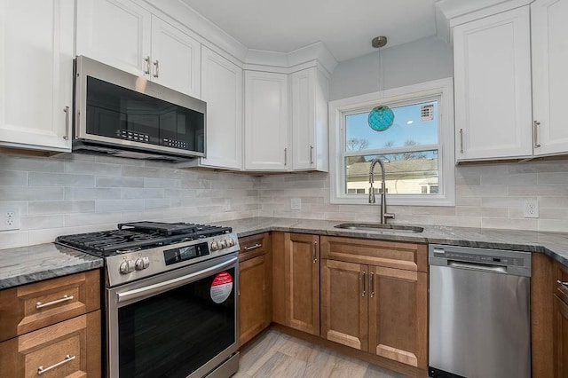 kitchen featuring a sink, appliances with stainless steel finishes, backsplash, brown cabinetry, and dark stone countertops