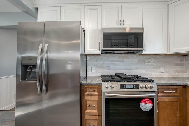 kitchen with tasteful backsplash, white cabinets, a wainscoted wall, stainless steel appliances, and stone counters