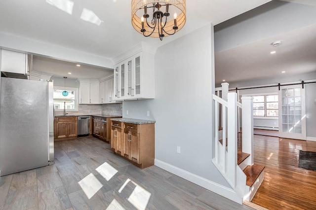 kitchen featuring a barn door, stainless steel appliances, white cabinets, decorative backsplash, and glass insert cabinets