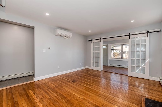 spare room featuring a wall unit AC, a baseboard radiator, hardwood / wood-style floors, a barn door, and baseboards